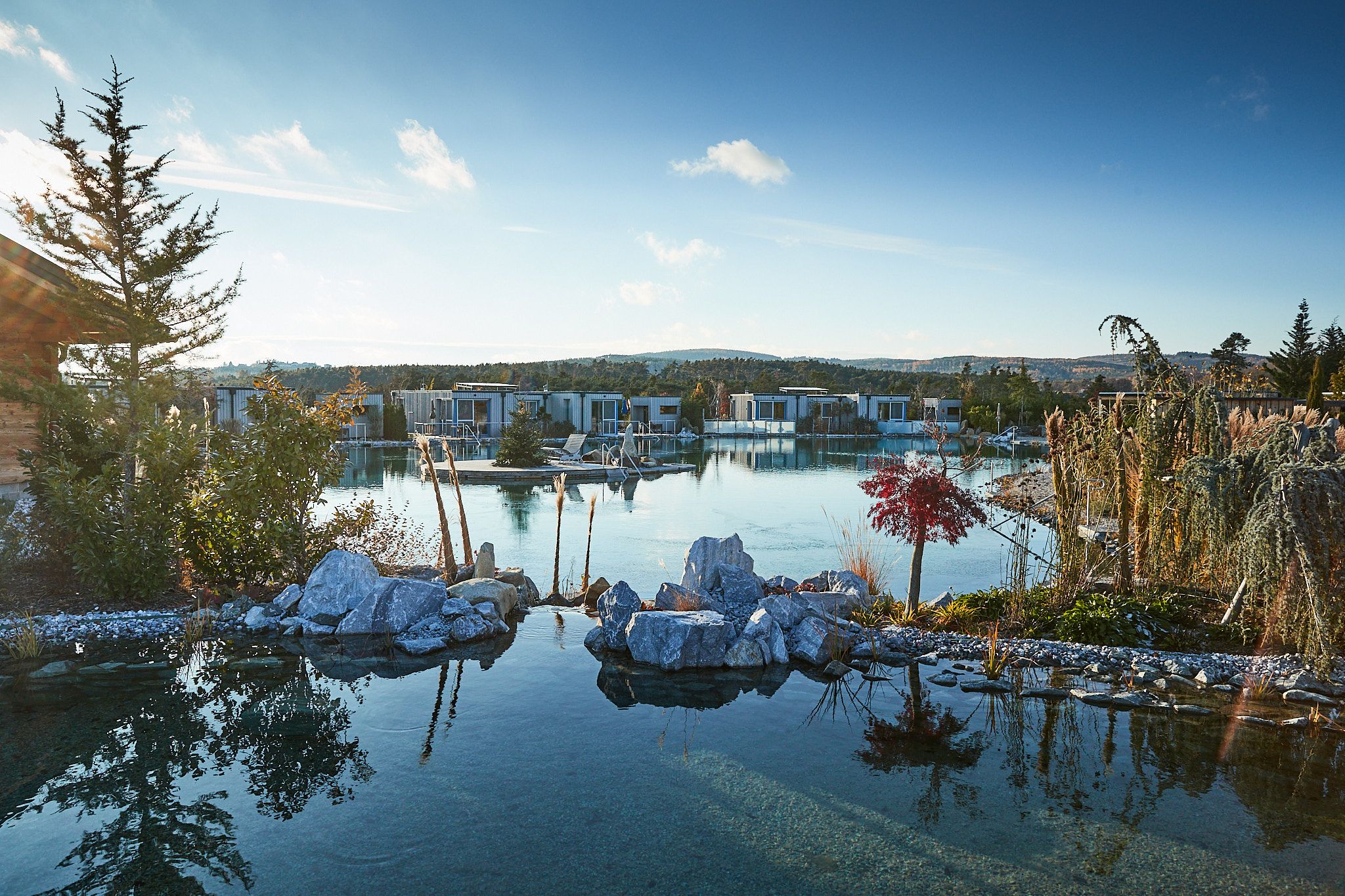 Blick über den Gartensee der von Steinen und Bäumen eingerahmt ist auf die Chalets direkt am See.