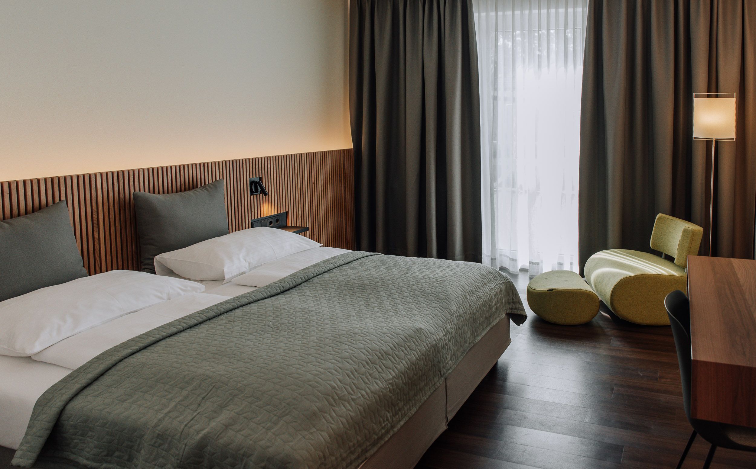 Modern eingerichtetes Hotelzimmer mit Doppelbett, grünem Sessel und Schreibtisch.
