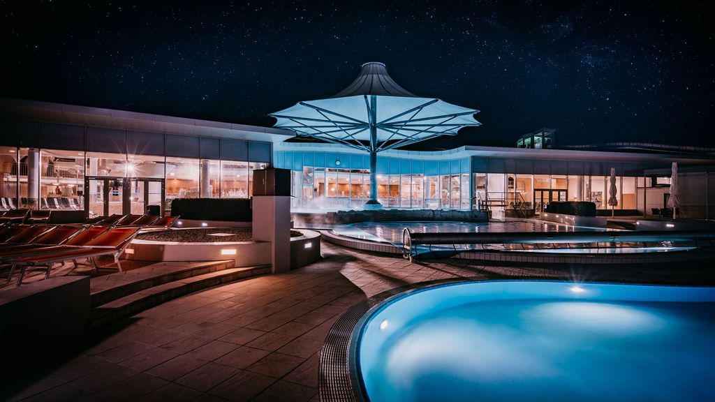 Nachtaufnahme eines modernen Spa-Bereichs mit beleuchteten Pools und einem großen Sonnenschirm.