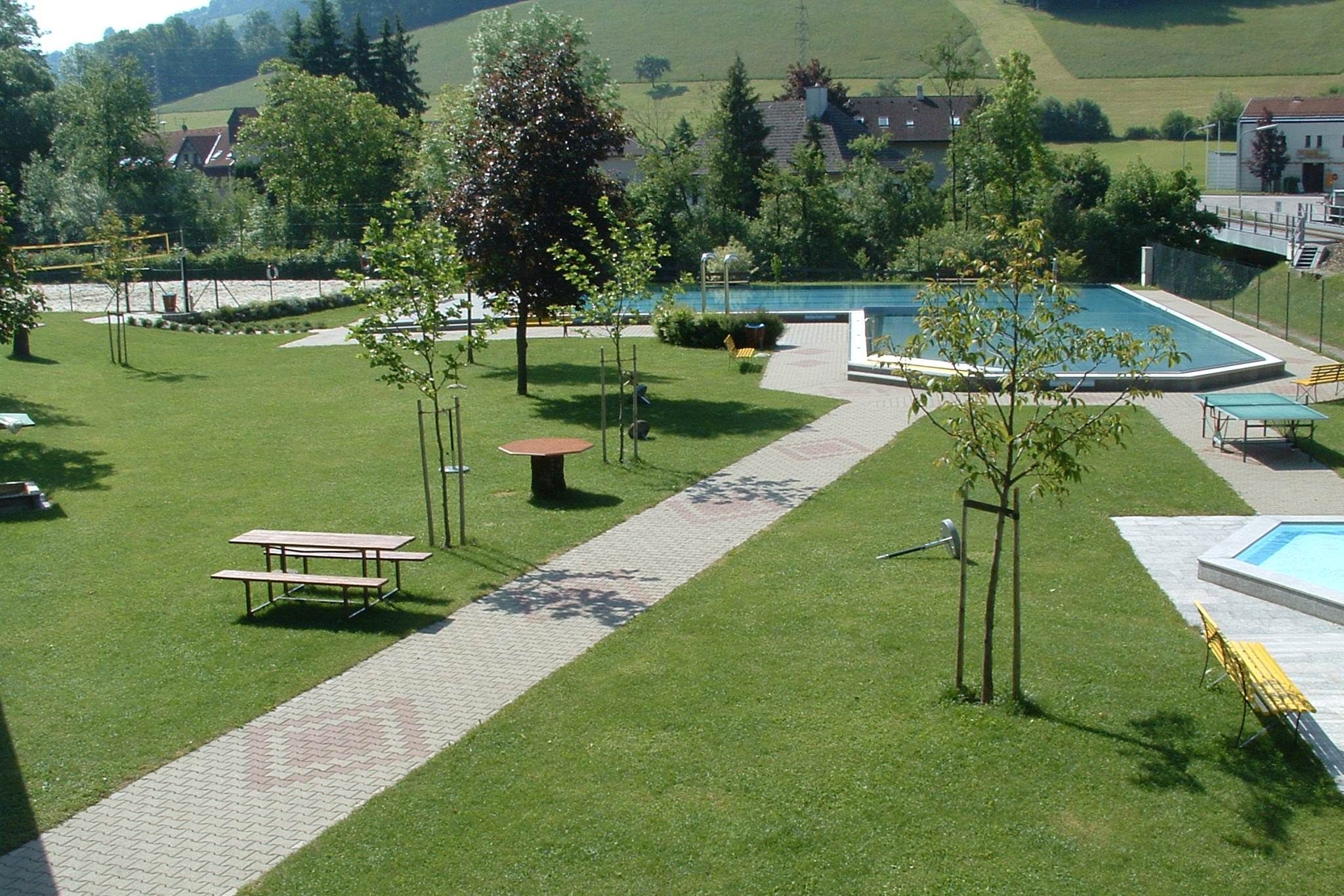 Grüne Parkanlage mit Schwimmbecken und Sitzbänken.