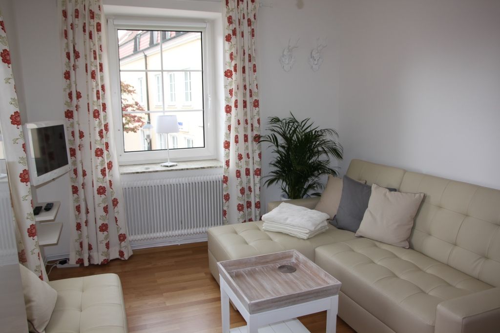 Helles Wohnzimmer mit beigem Sofa, Kissen, Couchtisch und Fenster mit Vorhängen.