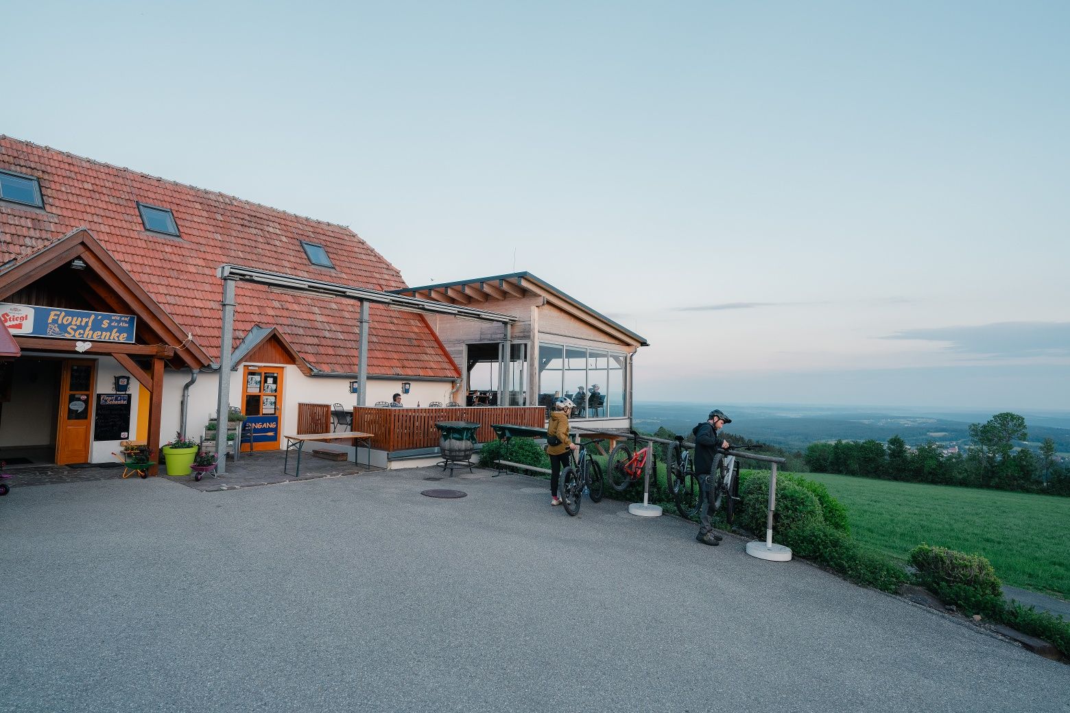 Ein Gasthaus mit Terrasse und Fahrradfahrern in einer ländlichen Umgebung.