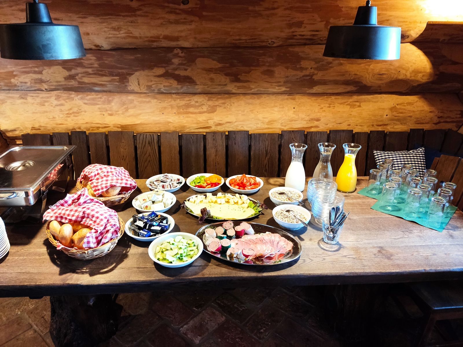 Frühstücksbuffet mit Brötchen, Aufschnitt, Käse, Gemüse, Müsli und Getränken auf einem Holztisch.