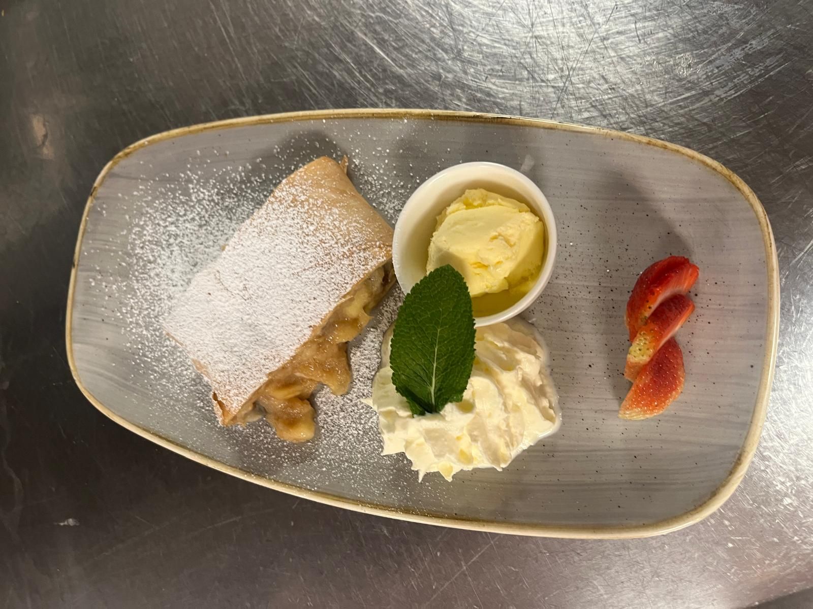 Ein Dessertteller mit Apfelstrudel, Vanilleeis, Sahne und Erdbeerscheiben.