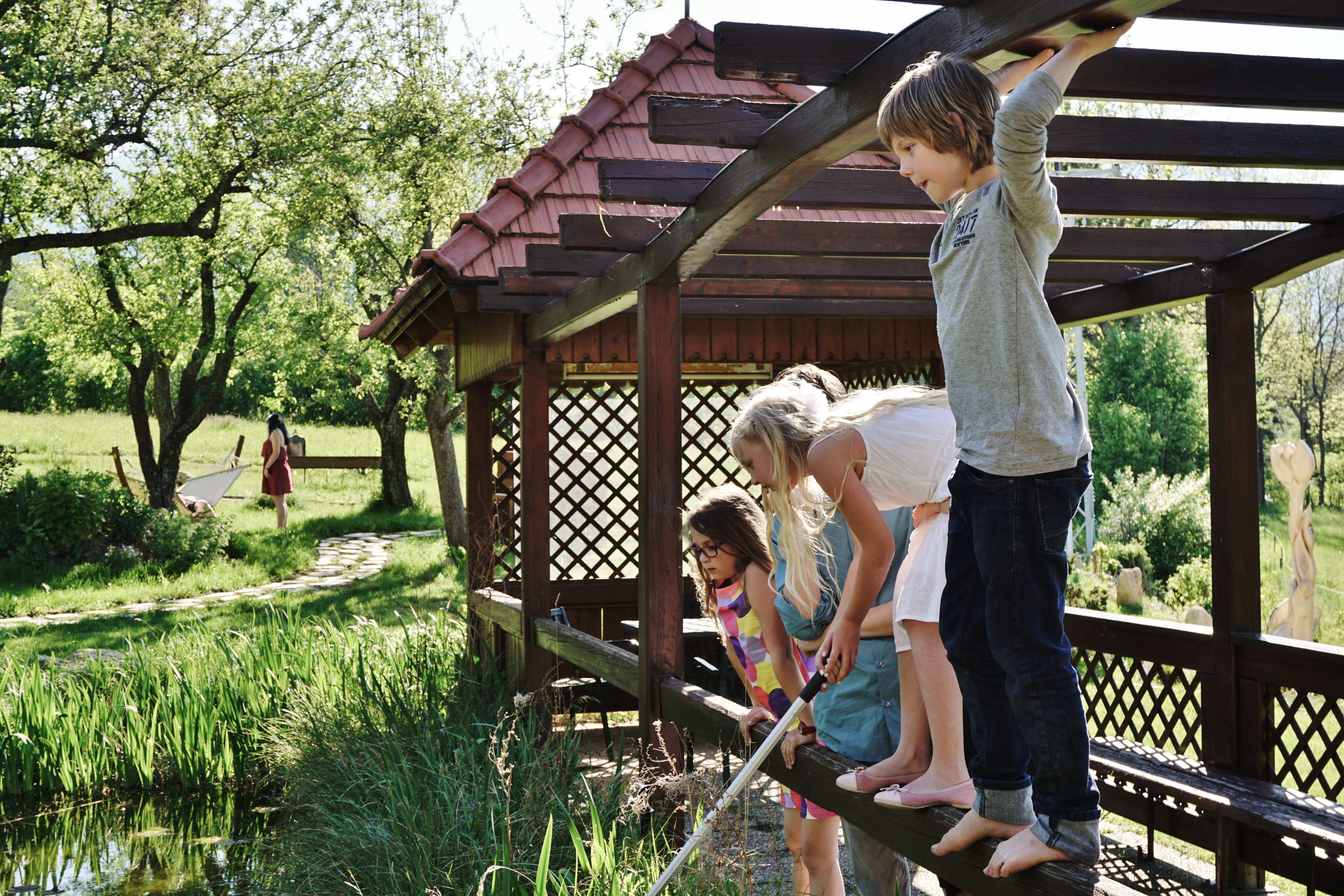 Kinder spielen auf einer Holzbrücke über einem Teich in einem Garten.