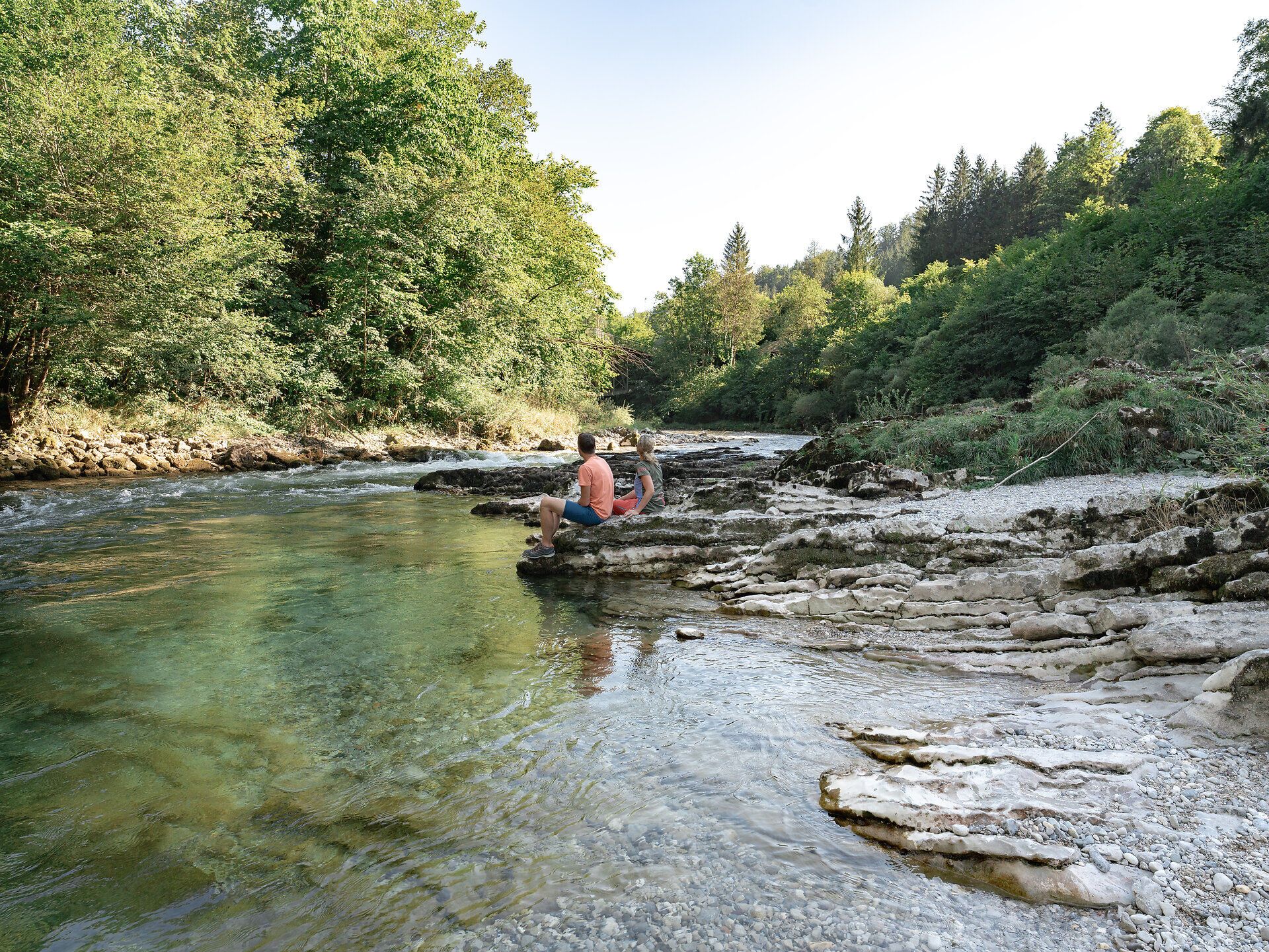 Ein sanfter Fluss schlängelt sich durch die malerische Landschaft, umgeben von üppigem Grün und majestätischen Bäumen. Die ruhige Atmosphäre lädt dazu ein, die Seele baumeln zu lassen und die Schönheit der Natur zu genießen.