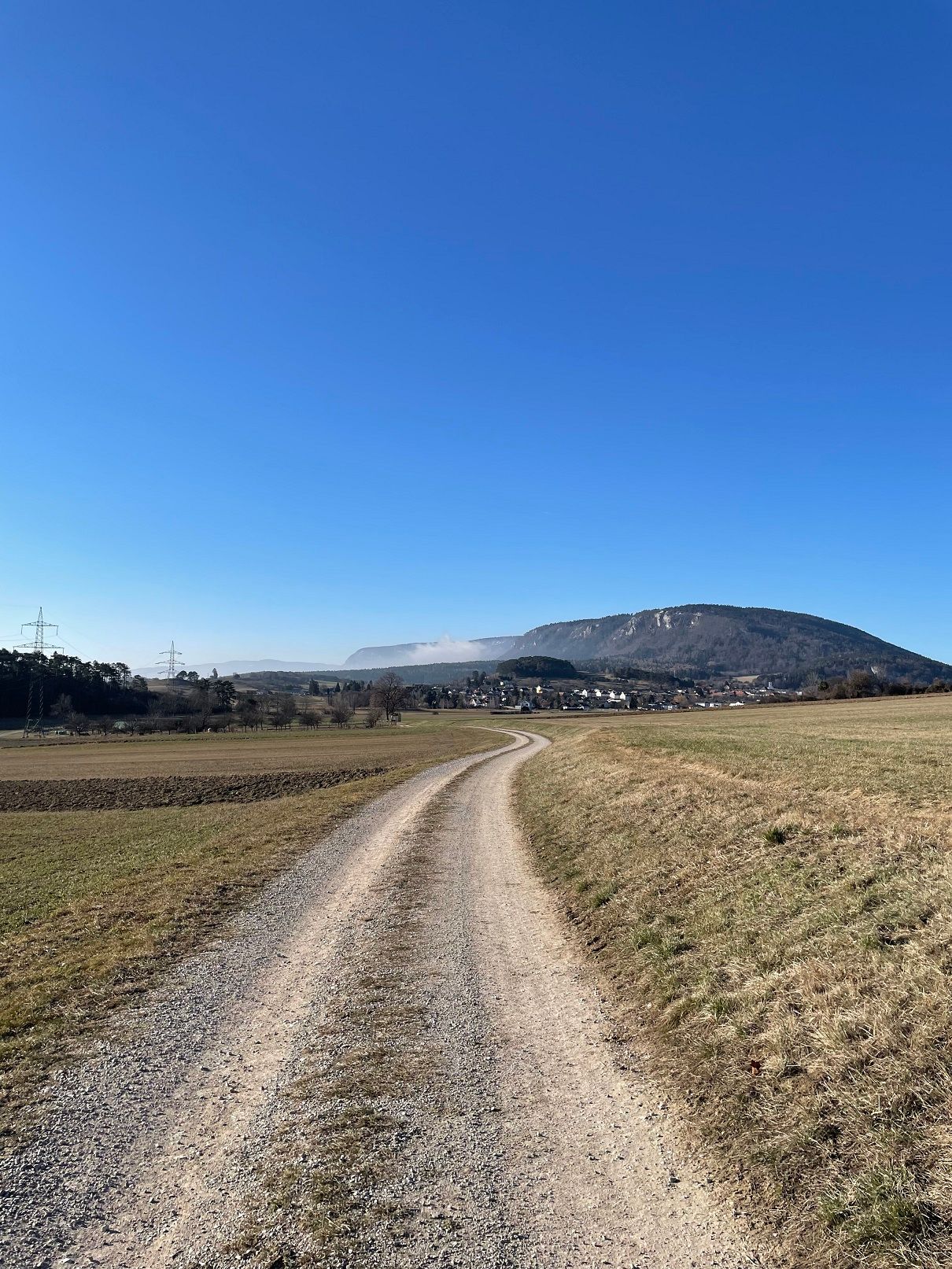 Landschaft mit Feldweg, Bergen und blauem Himmel.