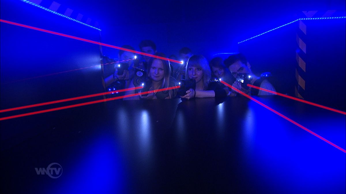 Menschen spielen Lasertag in einem dunklen Raum mit blauen Lichtern und roten Laserstrahlen.