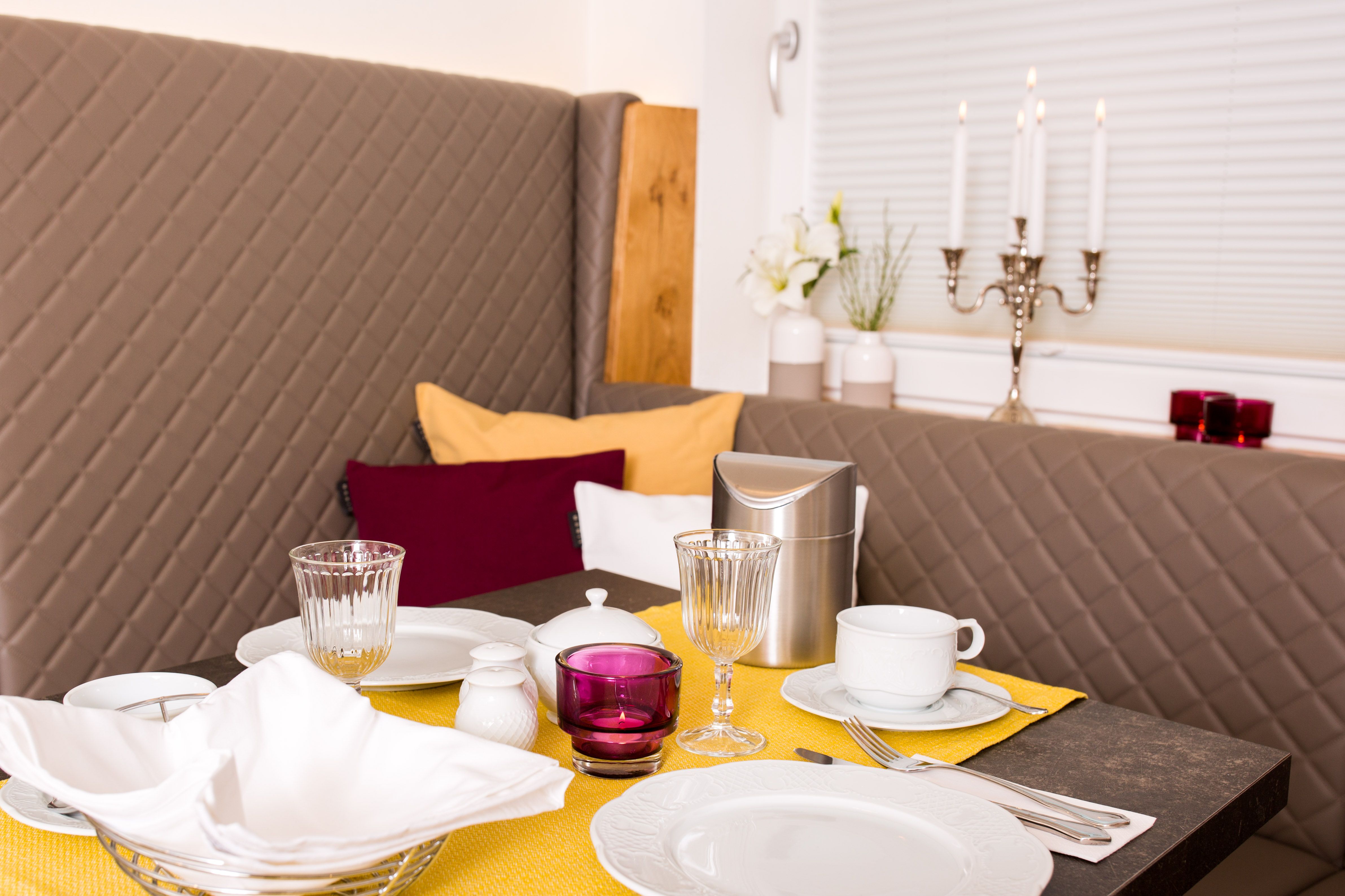 Eleganter Frühstückstisch mit gelbem Läufer, Geschirr, Gläsern und Kerzenleuchter.