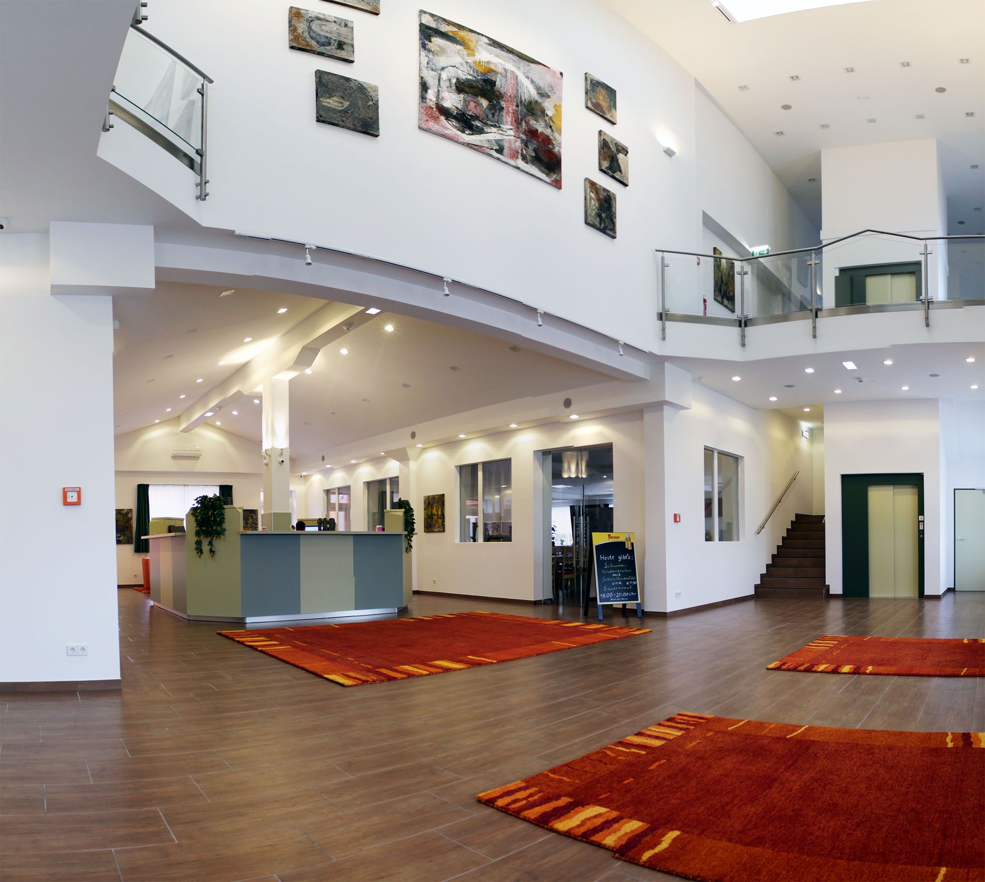 Moderne Hotellobby mit Rezeption, roten Teppichen und Kunstwerken an den Wänden.