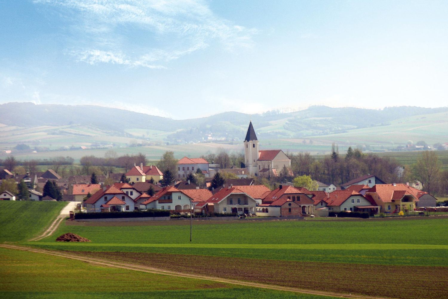 Panorama von Großharras mit Kirche und Hügeln im Hintergrund.