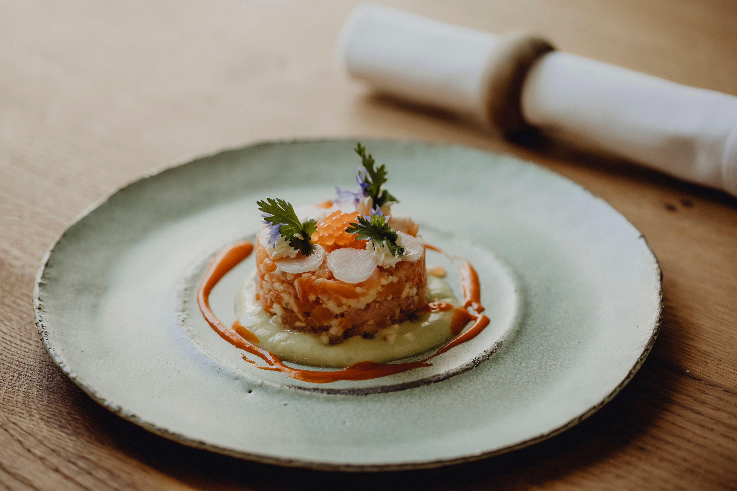 Gourmetgericht auf einem Teller mit Lachs, Kräutern und Soße dekoriert.