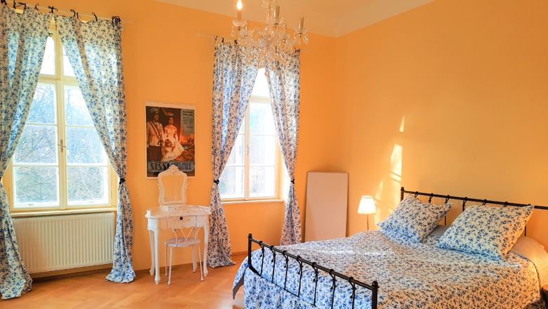 Ein gemütliches Schlafzimmer mit einem Bett, blauen Blumenmustern, einem Schminktisch und einem Kronleuchter.