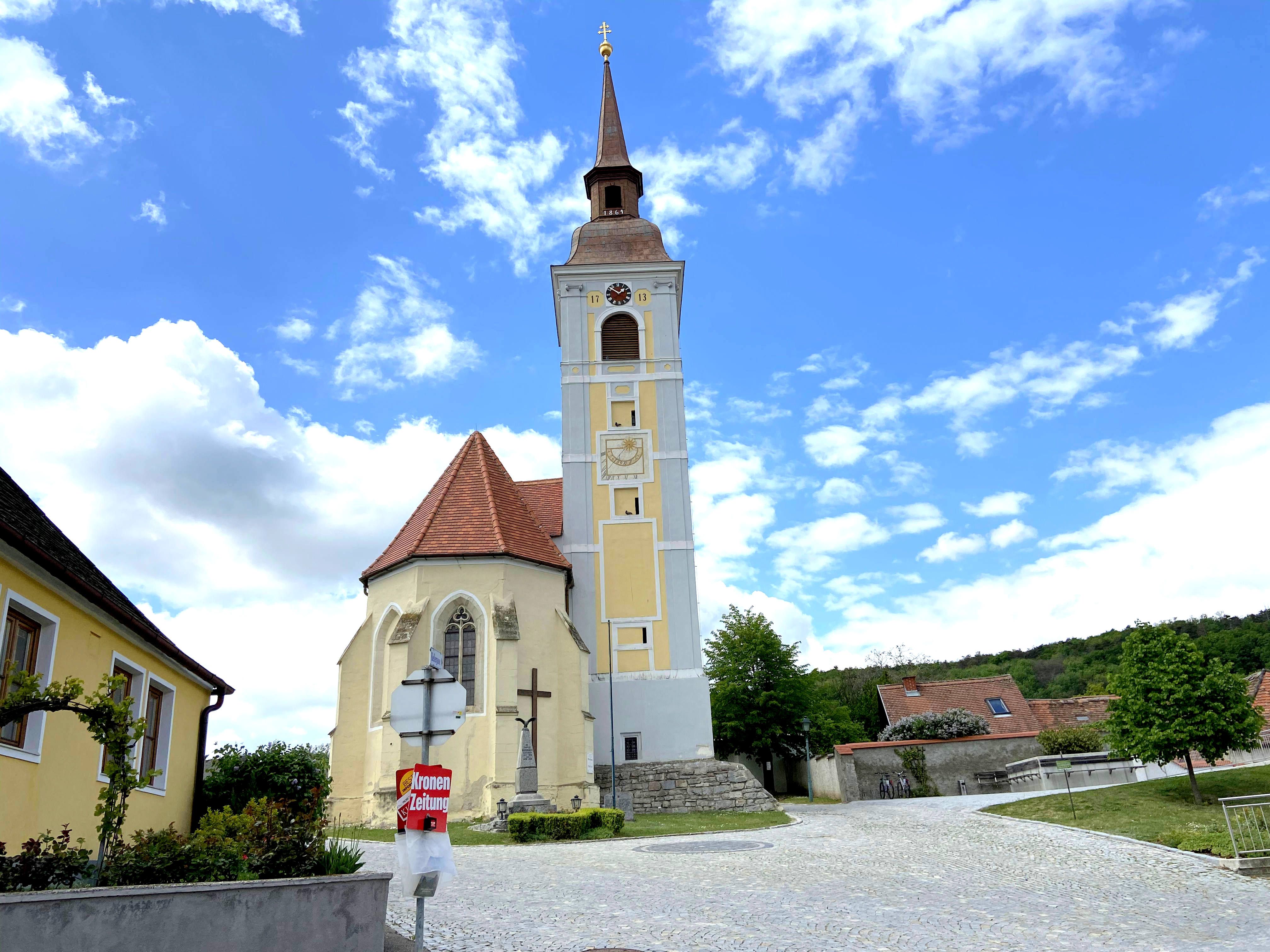 Kirche mit schiefem Turm in Waitzendorf, umgeben von blauen Himmel und Wolken.