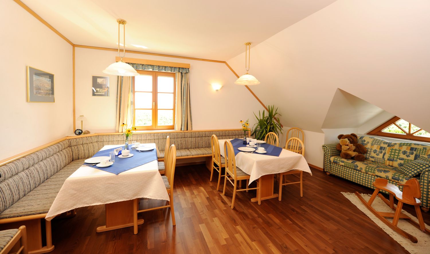 Gemütlicher Frühstücksbereich mit Holzmöbeln, gedeckten Tischen und einem Sofa mit Teddybären.