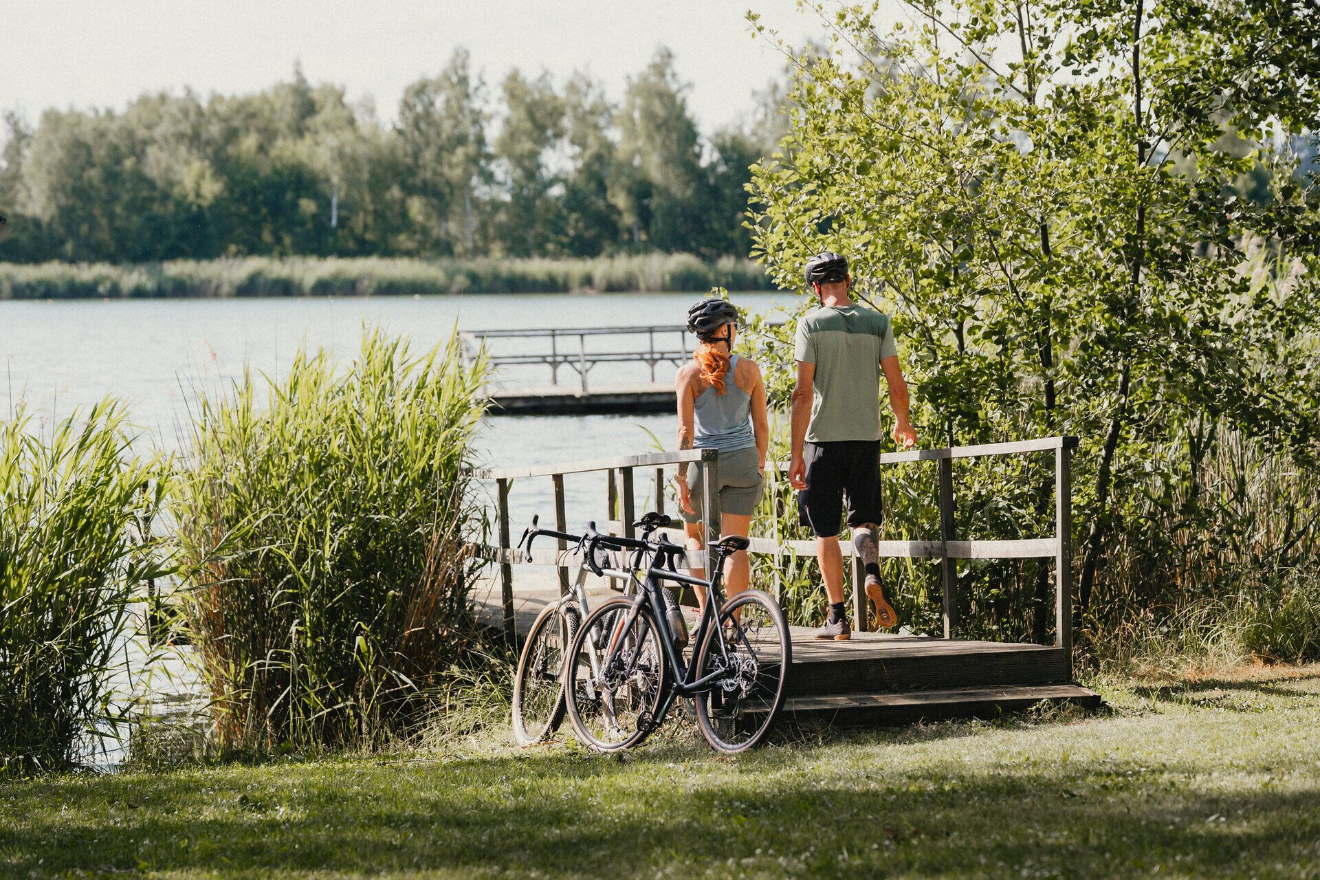 Zwei Personen gehen Richtung Bergwerksee entlang eines Stegs, ihre Räder haben sie vorher abgestellt