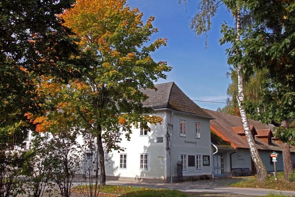 Ein weißes Gebäude mit der Aufschrift 'Heimatmuseum', umgeben von Bäumen mit Herbstlaub.