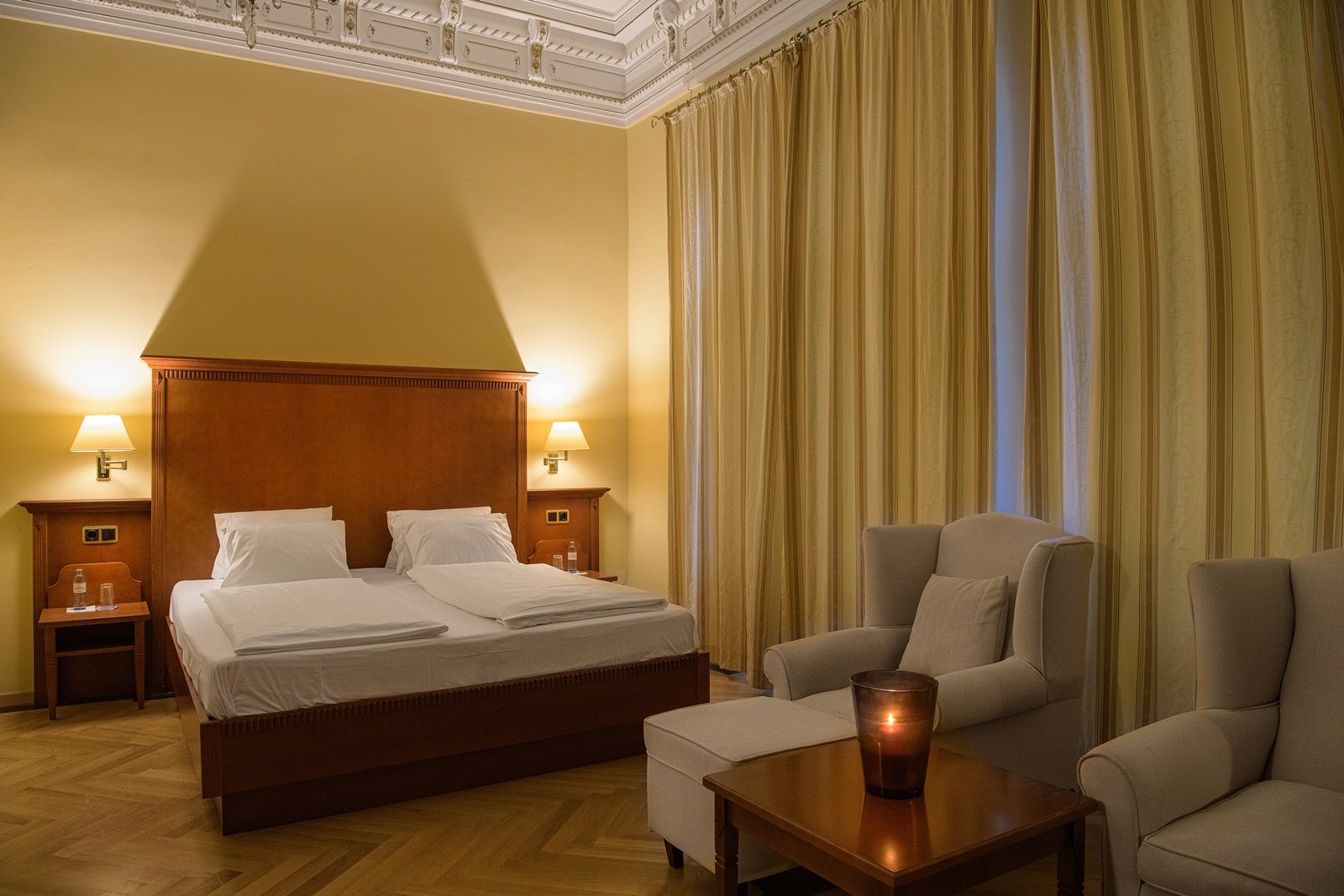 Elegantes Doppelzimmer mit großem Bett, zwei Sesseln und einem Tisch mit Kerze.