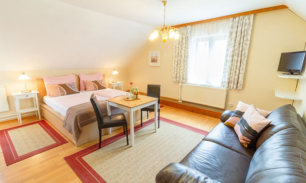 Gemütliches Gästezimmer mit Doppelbett, Sofa, Tisch und Stühlen, helle Einrichtung.