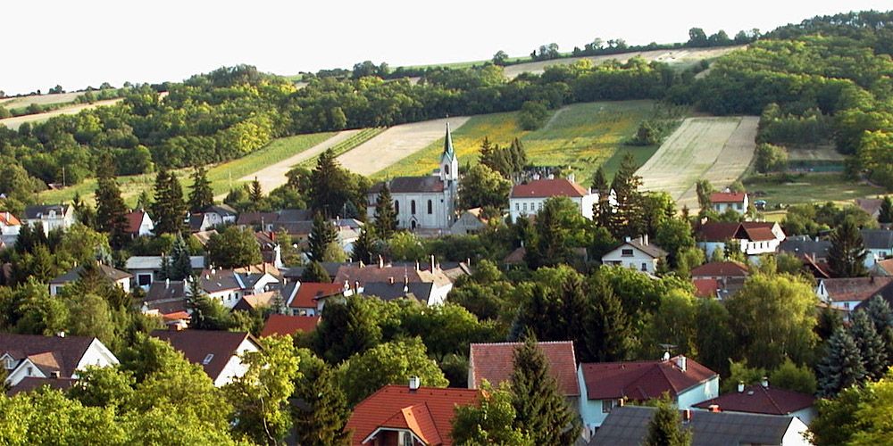 Panorama von Unterolberndorf mit Kirche und umliegenden Häusern vor grünen Hügeln.