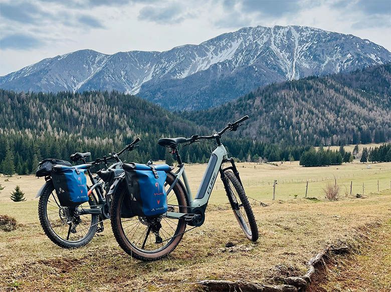 Zwei Mountainbikes mit blauen Taschen vor einer Berglandschaft im Schneebergland.