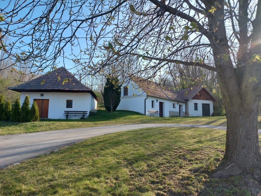 Weiße Gebäude mit roten Dächern in ländlicher Umgebung, Bäume im Vordergrund.
