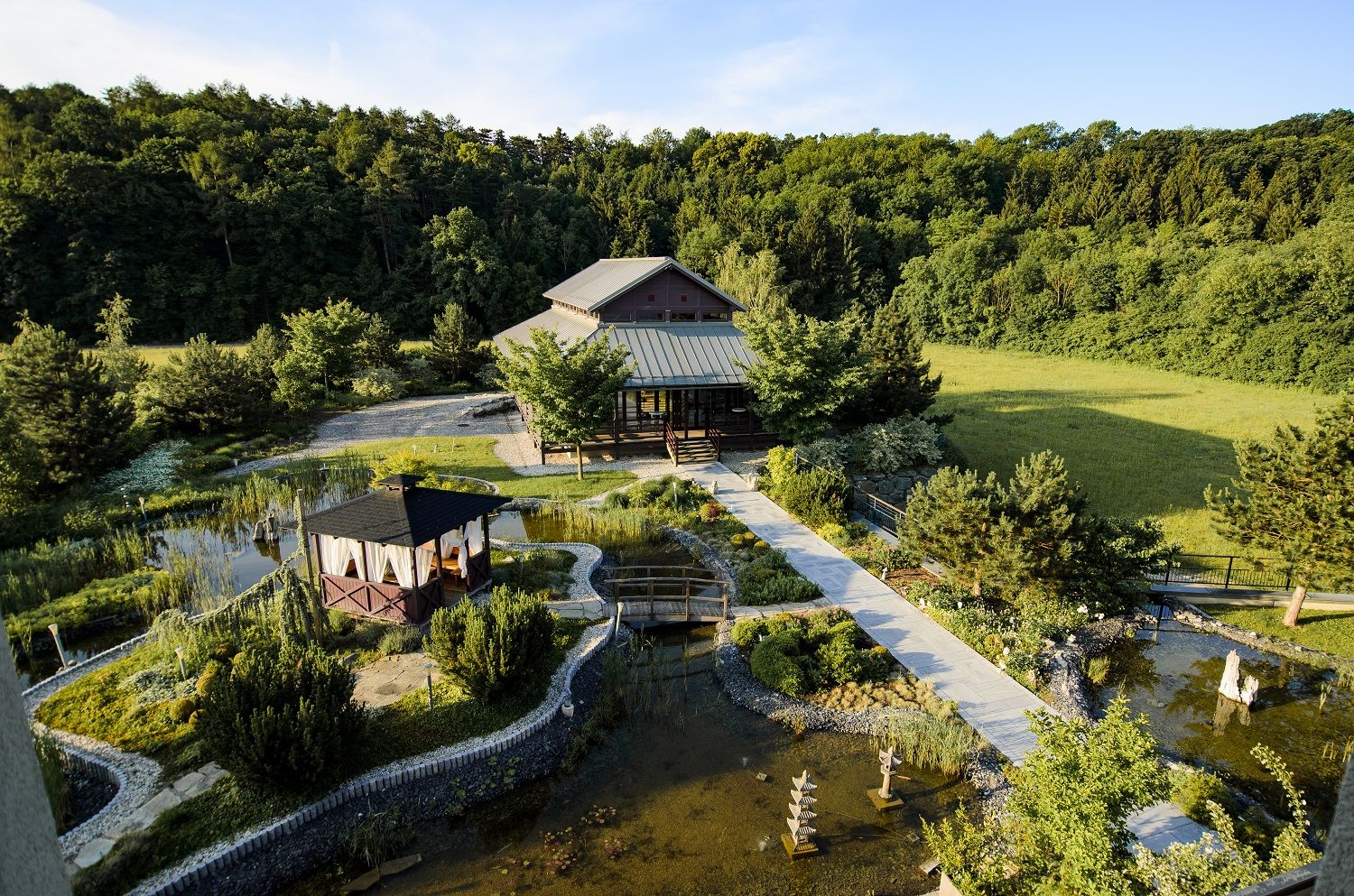 Asiatisch gestalteter Garten mit Pavillon und Teich, umgeben von Wald.
