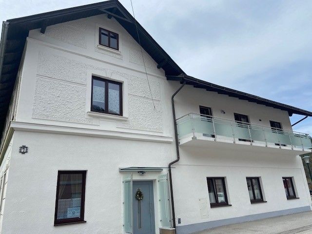 Zweistöckiges weißes Haus mit Balkon und mehreren Fenstern.