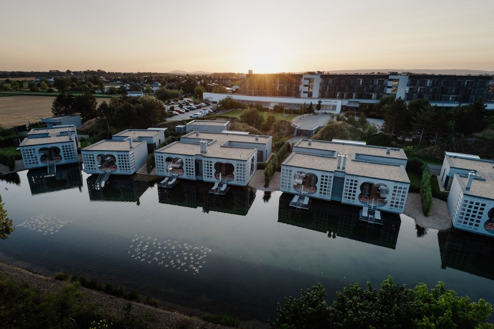 Luftaufnahme von modernen Gebäuden am Wasser im Thermenresort Laa bei Sonnenuntergang.