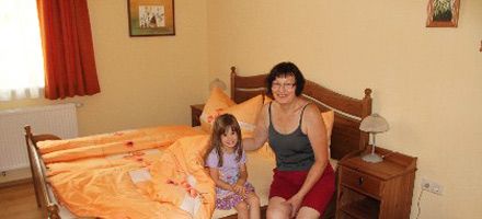 Eine Frau und ein Kind sitzen auf einem Bett in einem Gästezimmer mit orangefarbener Bettwäsche.