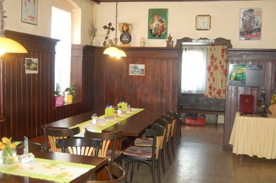 Gemütlicher Gastraum mit Holztäfelung, Tisch mit Stühlen, dekorativen Postern und einer Uhr an der Wand.
