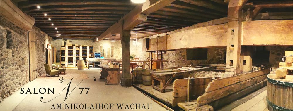 Innenansicht eines rustikalen Weinkellers mit Holzbalken und Steinwänden, beschriftet mit 'Salon 77 am Nikolaihof Wachau'.