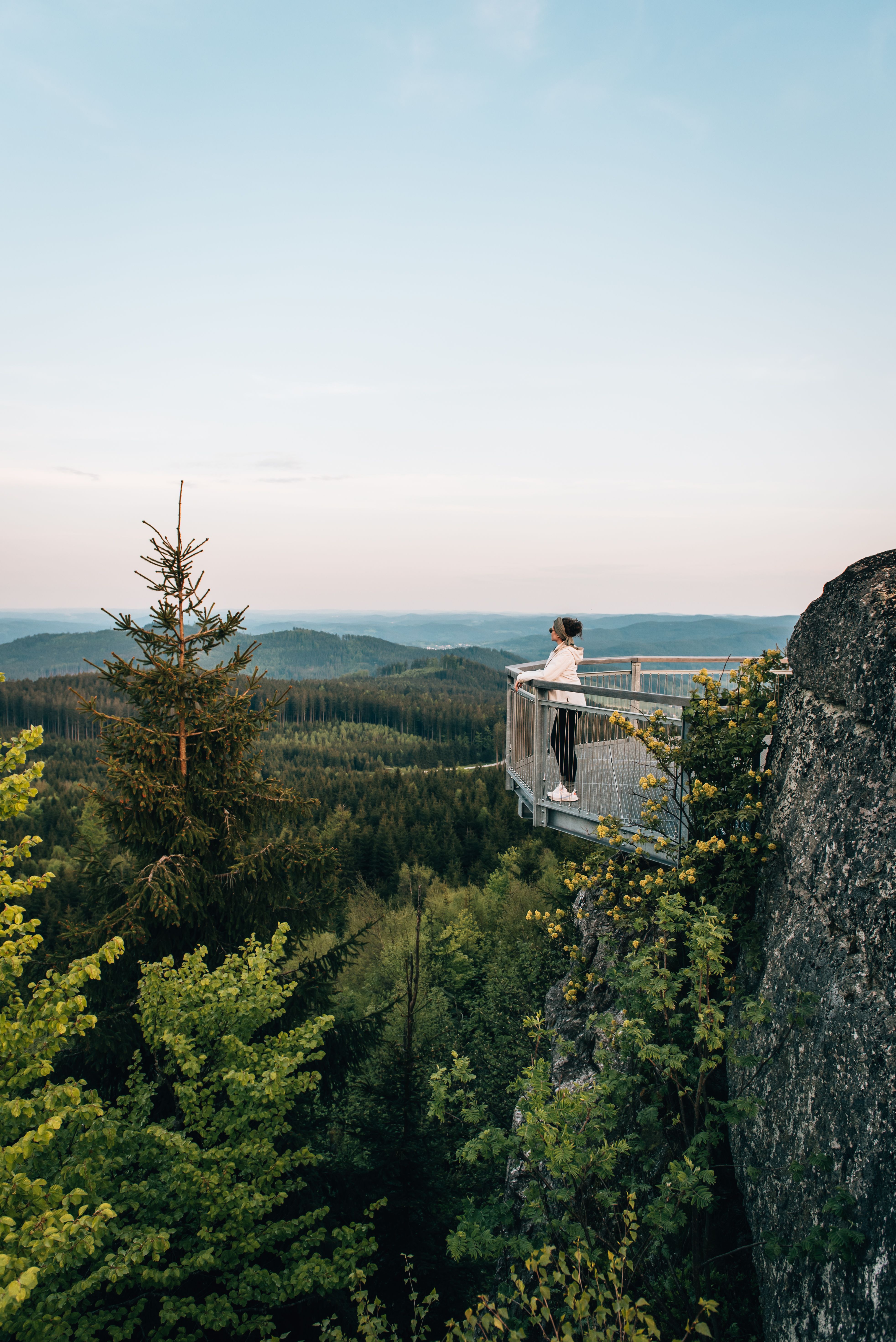 Ein atemberaubender Ausblick eröffnet sich über die sanften Hügel und dichten Wälder, während die Abendsonne den Himmel in sanften Pastelltönen färbt. Die frische Bergluft und das sanfte Rascheln der Blätter laden dazu ein, einen Moment innezuhalten und die Schönheit der Natur zu genießen.