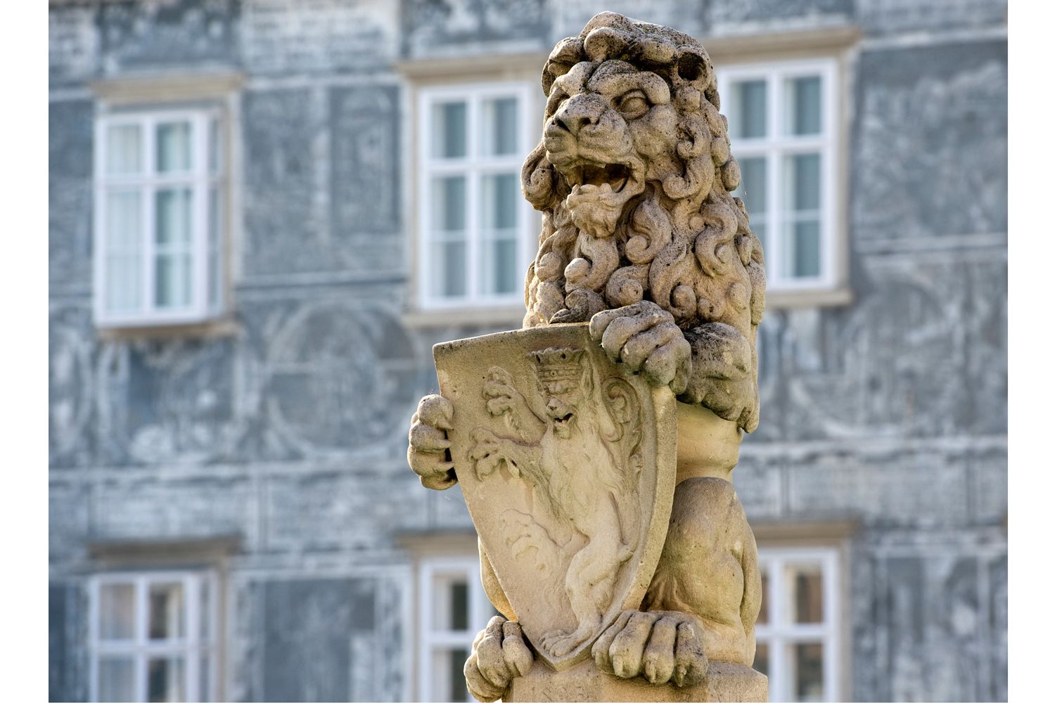 Steinlöwe mit Wappen auf einem Brunnen vor einem Gebäude.