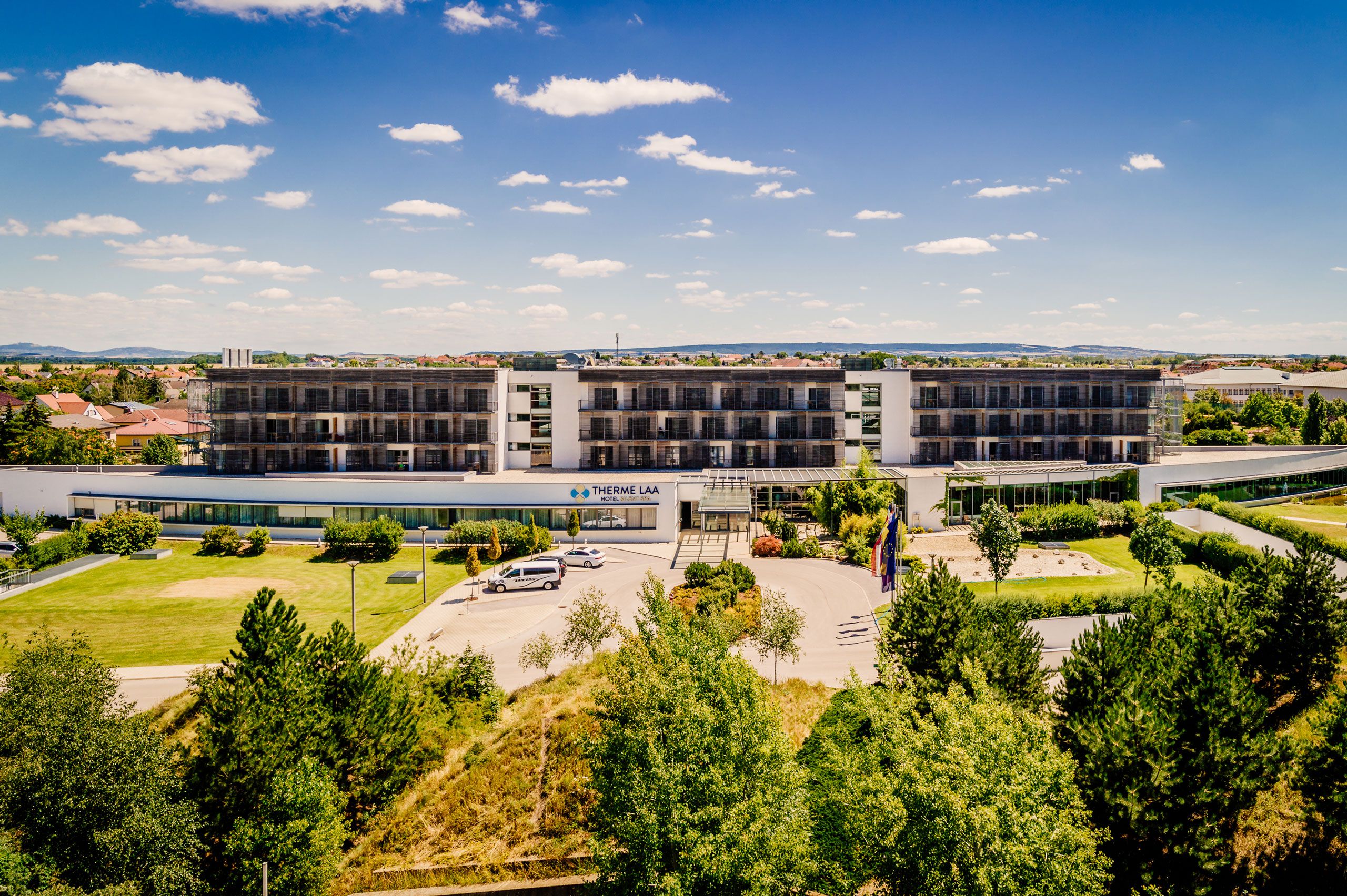 Außenansicht des Therme Laa Hotels mit grünem Garten und blauem Himmel.