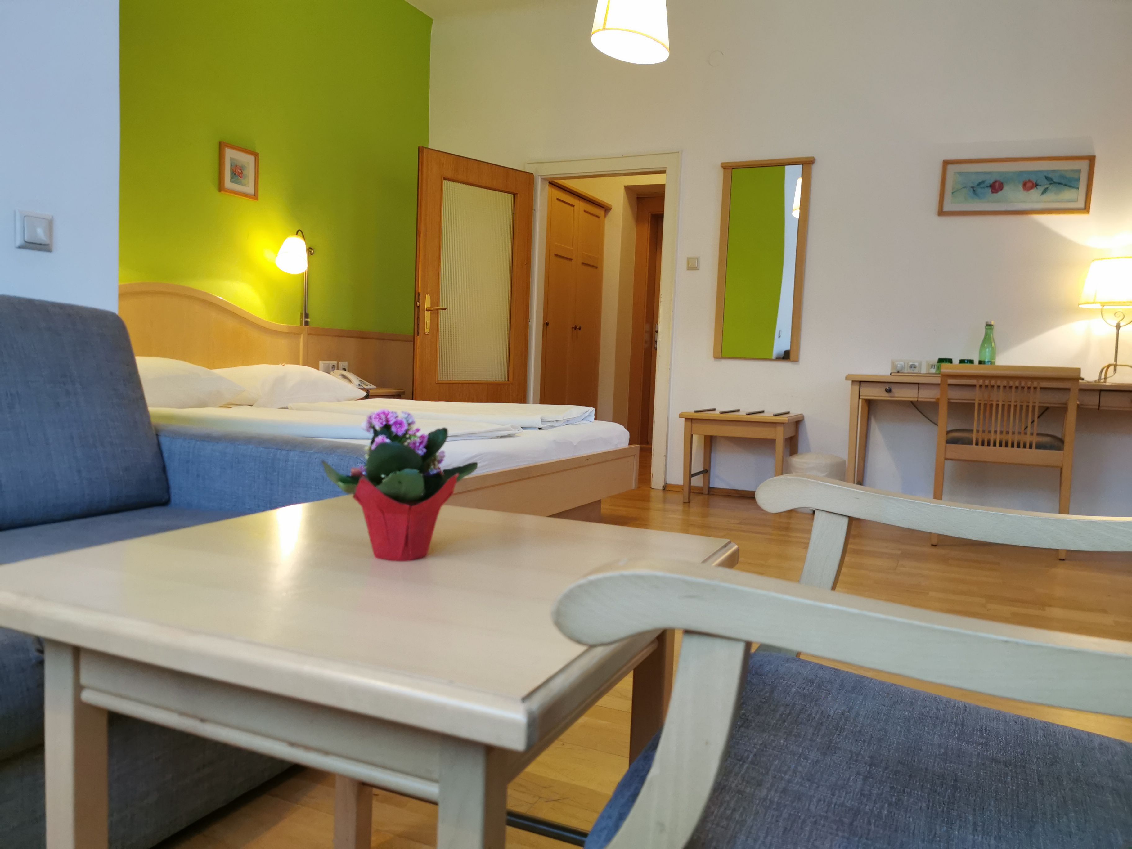 Hotelzimmer mit grünem Akzent, Bett, Schreibtisch und Sessel.