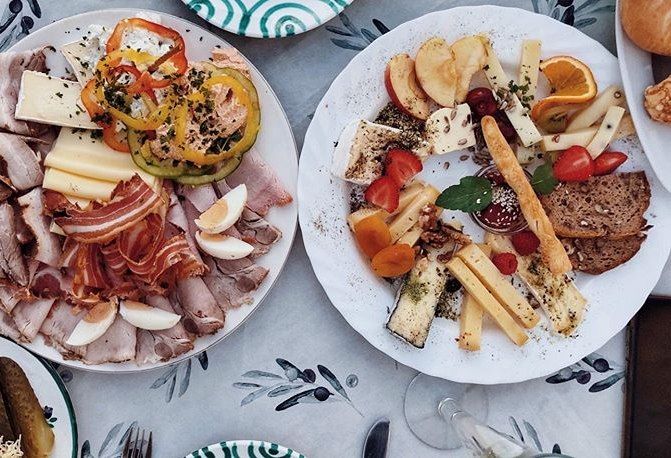 Zwei Teller mit Aufschnitt, Käse, Gemüse und Obst auf einem Tisch.