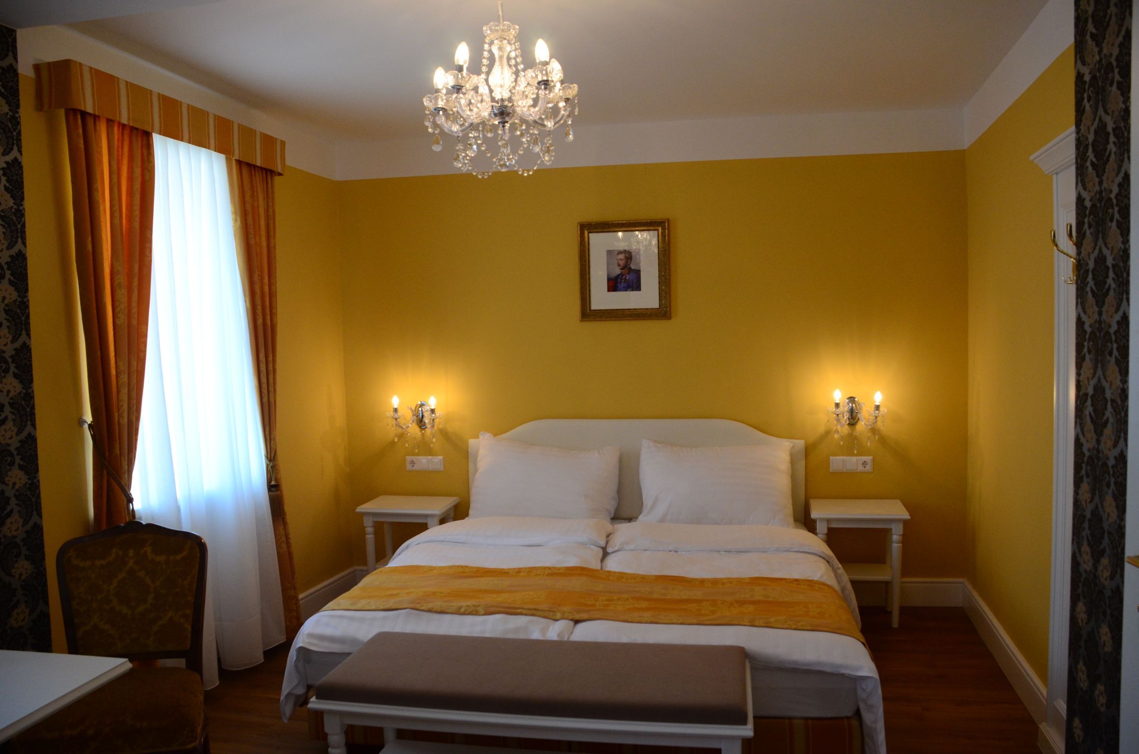 Elegantes Hotelzimmer mit gelben Wänden, Doppelbett, Kronleuchter und Bild an der Wand.