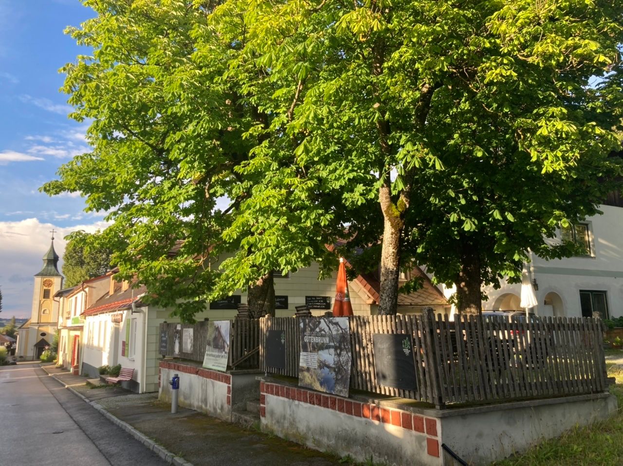 Ein traditionelles Wirtshaus mit einem Kastaniengarten und einer Kirche im Hintergrund.
