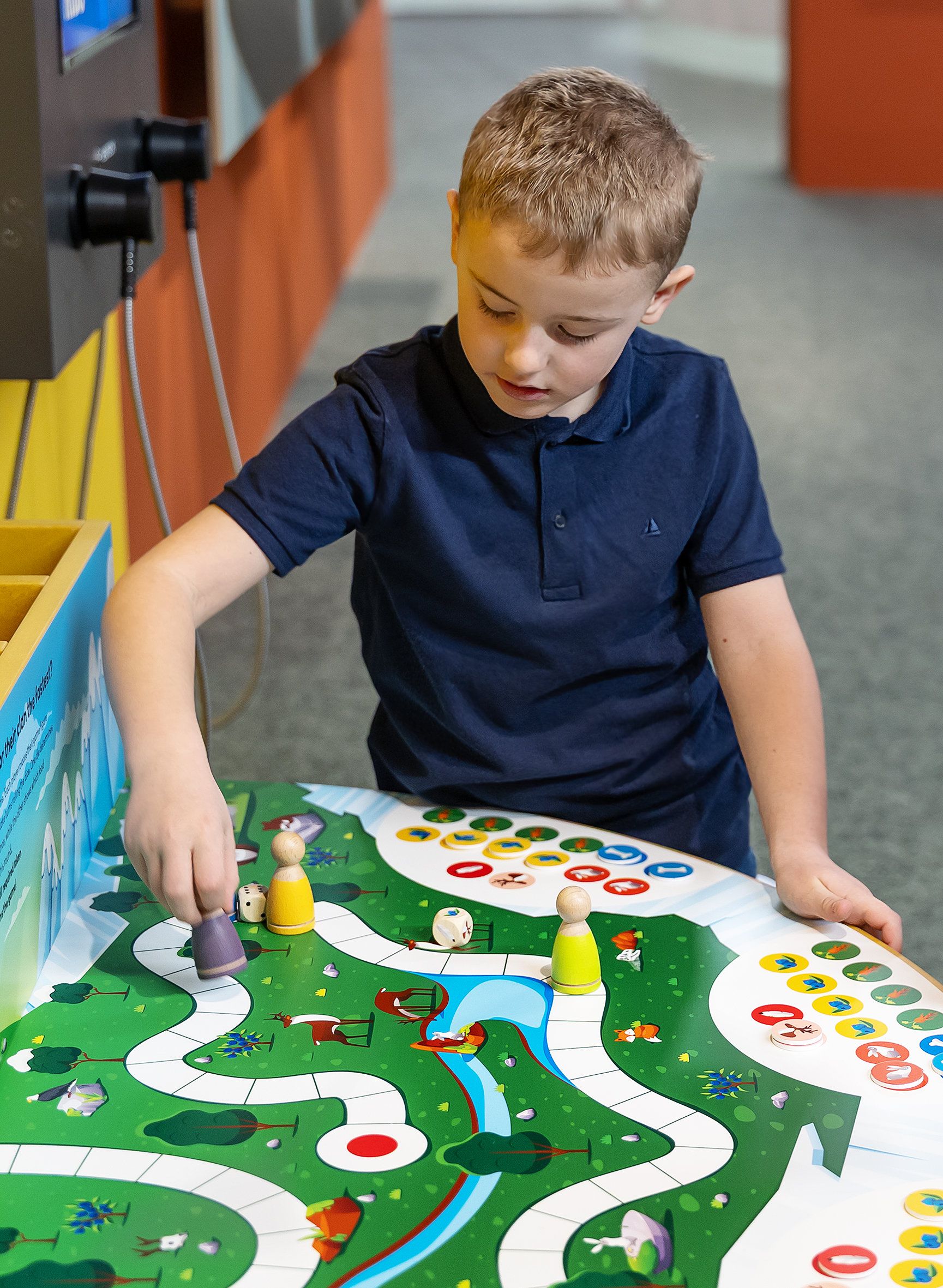 Ein Kind spielt ein Brettspiel mit bunten Spielfiguren und Würfeln auf einem Tisch.