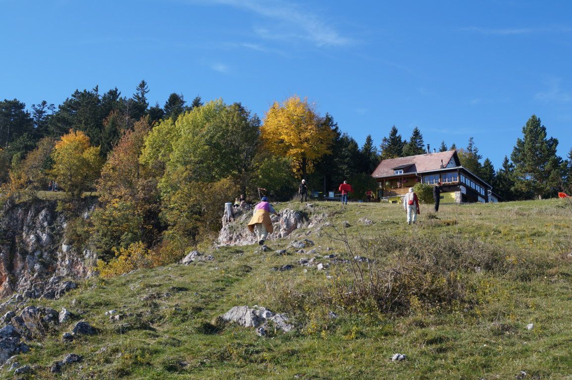 Menschen wandern auf einem grasbewachsenen Hügel mit einer Berghütte im Hintergrund.