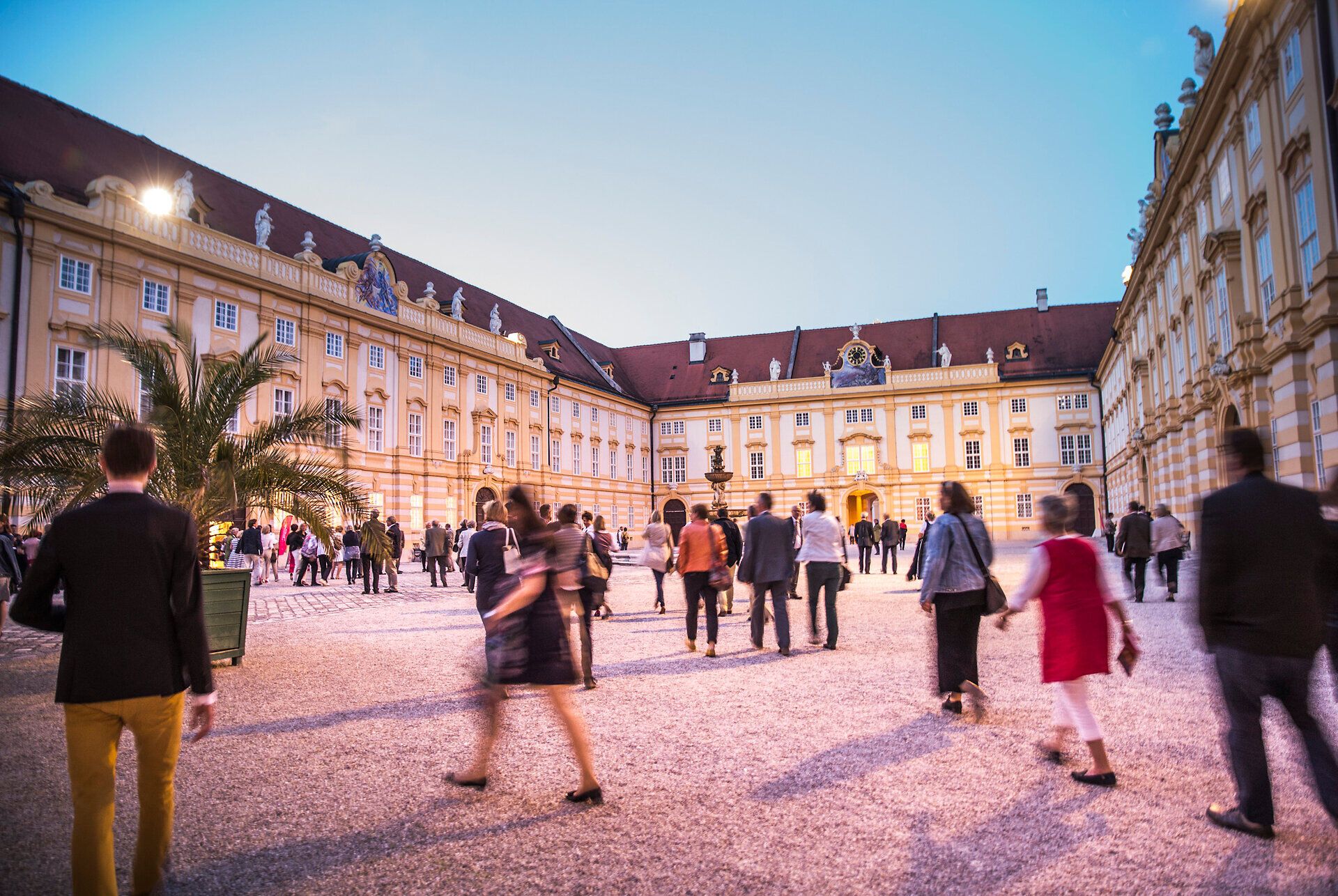 Die Barocktage im Stift Melk ziehen zahlreiche Besucher an, die in festlicher Stimmung durch den malerischen Innenhof schlendern. Die sanften Farben des Abendhimmels und die beeindruckende Architektur schaffen eine zauberhafte Atmosphäre, die zum Verweilen einlädt.