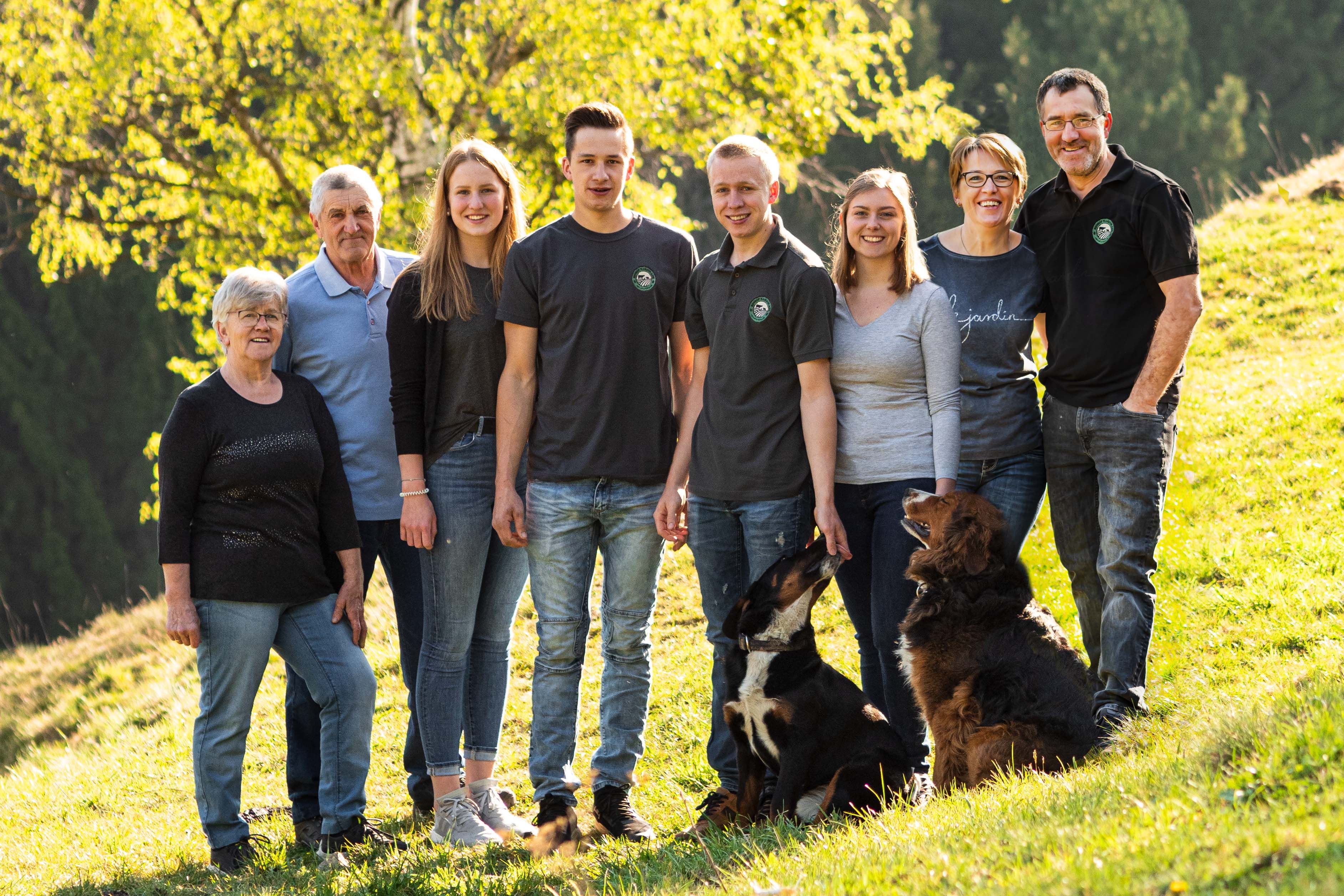 Eine große Familie mit zwei Hunden steht auf einer grünen Wiese vor einem Baum.