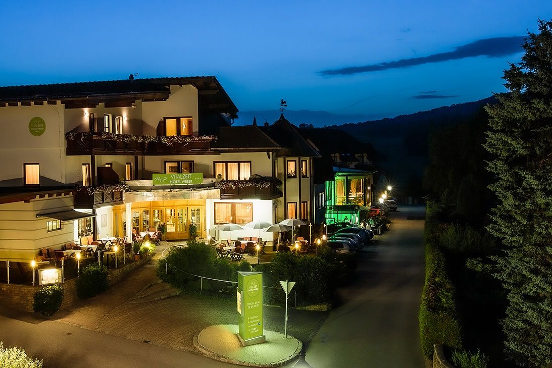 Außenansicht des Vitalzeit Hotel Weber bei Nacht, beleuchtet mit warmem Licht, umgeben von Bäumen und geparkten Autos.