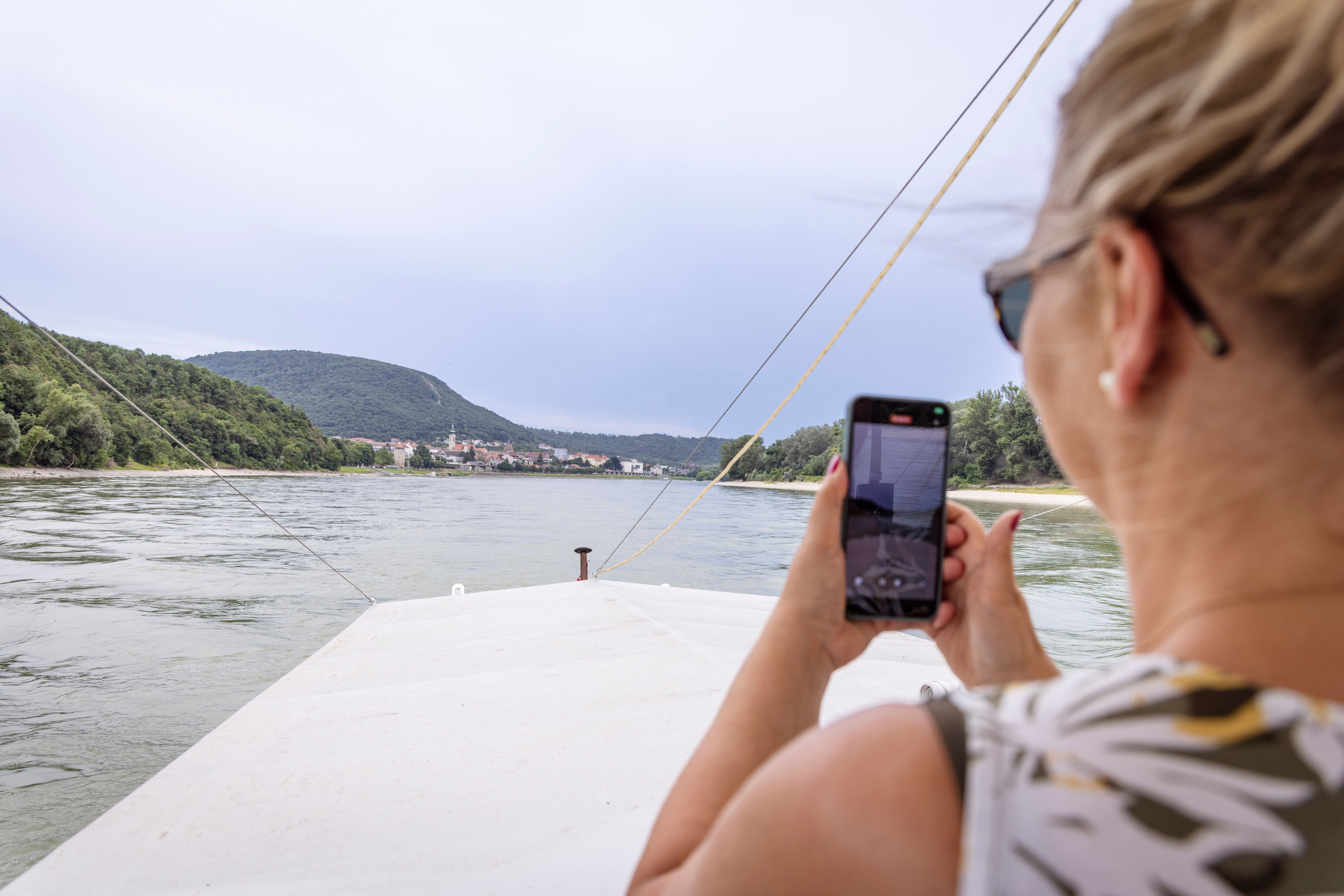 Frau auf einem Boot fotografiert die Donau mit ihrem Handy.