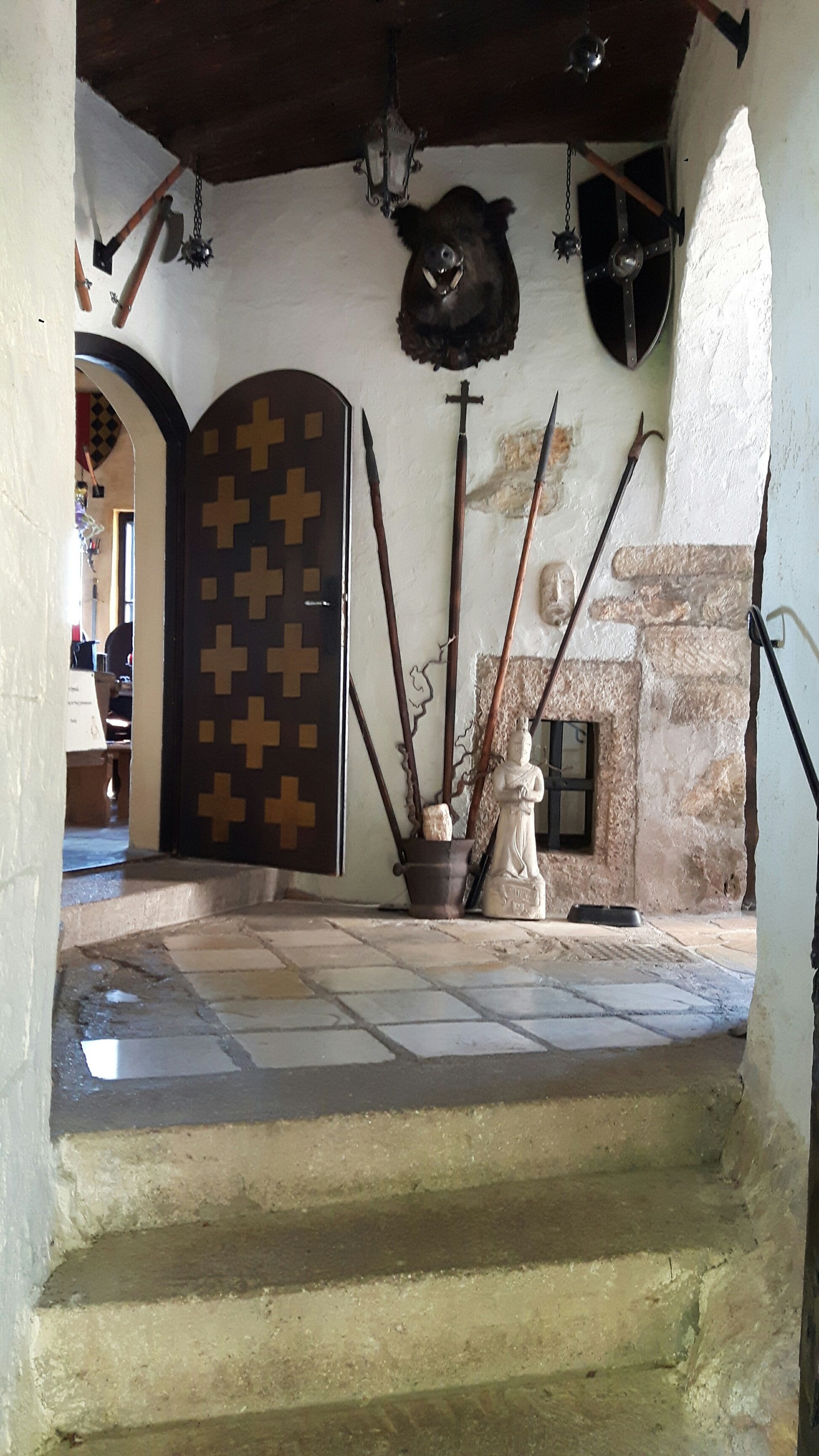 Innenansicht einer Burg mit Waffen, einem Wildschweinkopf und einer Statue.