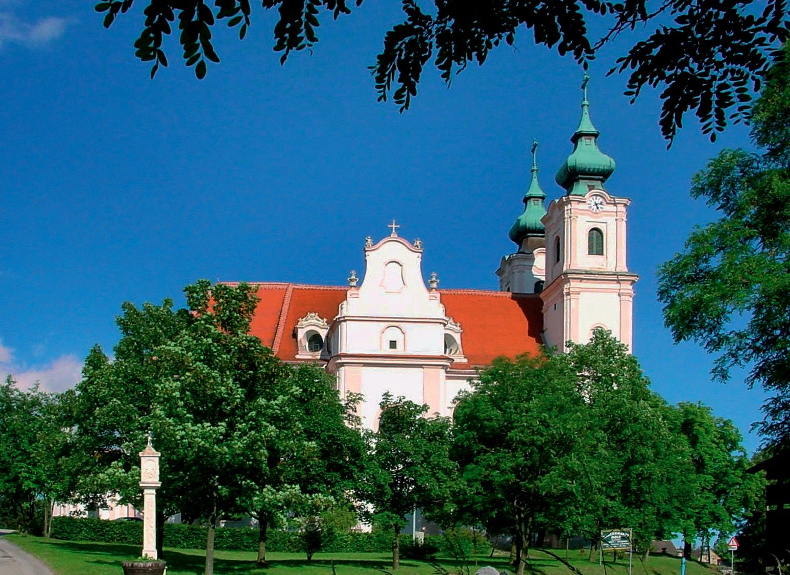 Basilika Maria Dreieichen mit roten Dächern und grünen Türmen, umgeben von Bäumen.