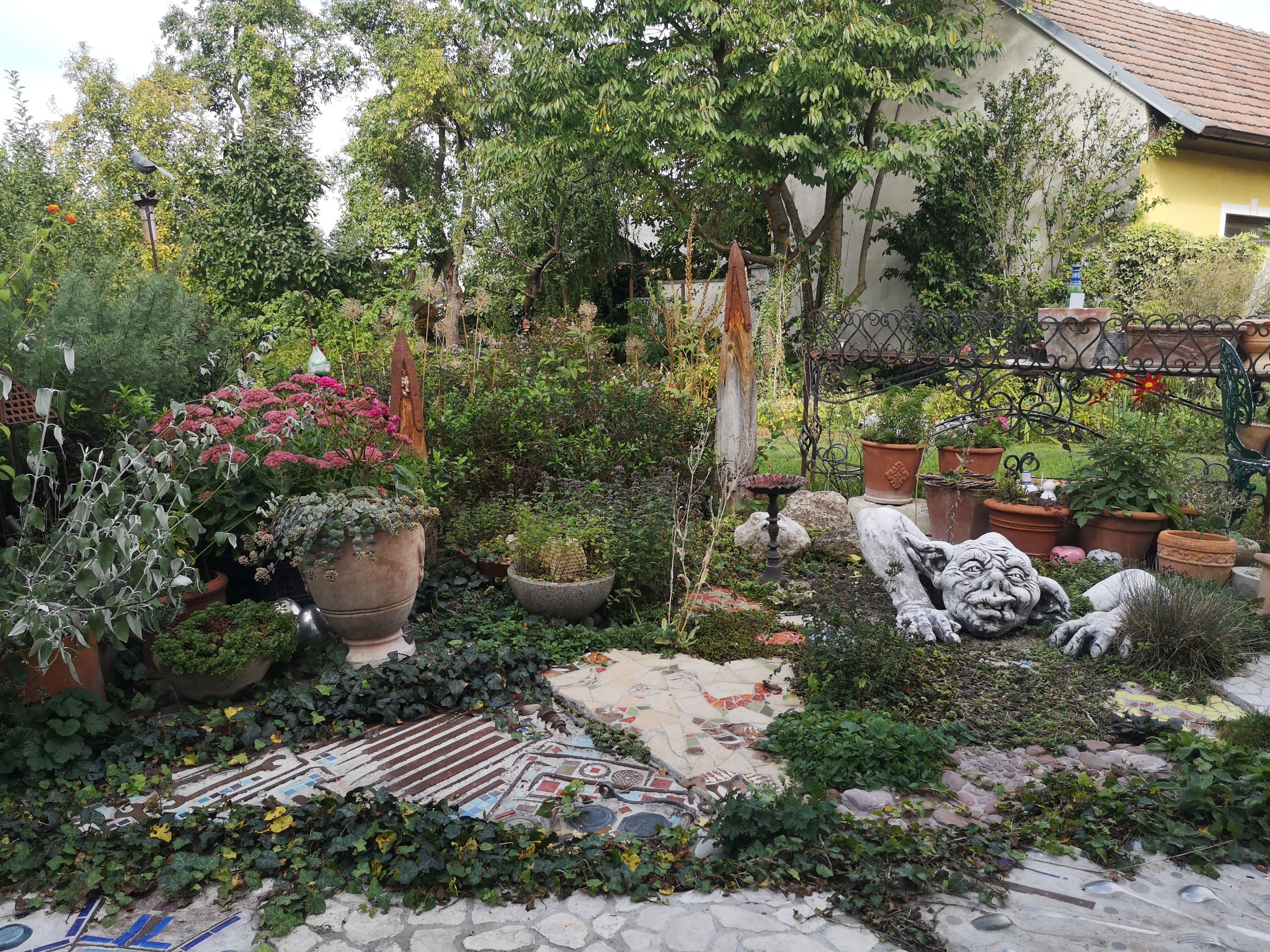 Ein Garten mit Pflanzen, Töpfen und einer grotesken Steinskulptur.