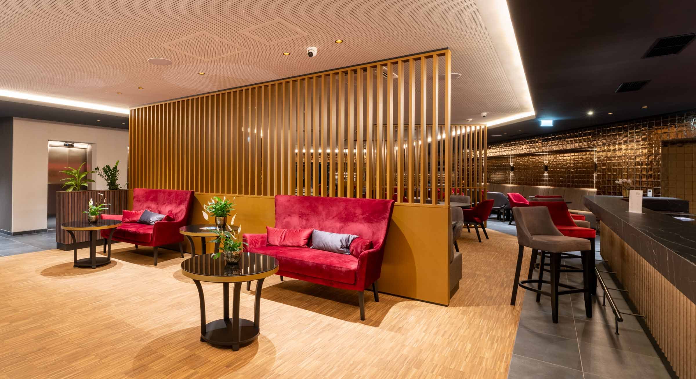 Moderne Hotellobby mit roten Sofas, Holzwänden und Pflanzen.