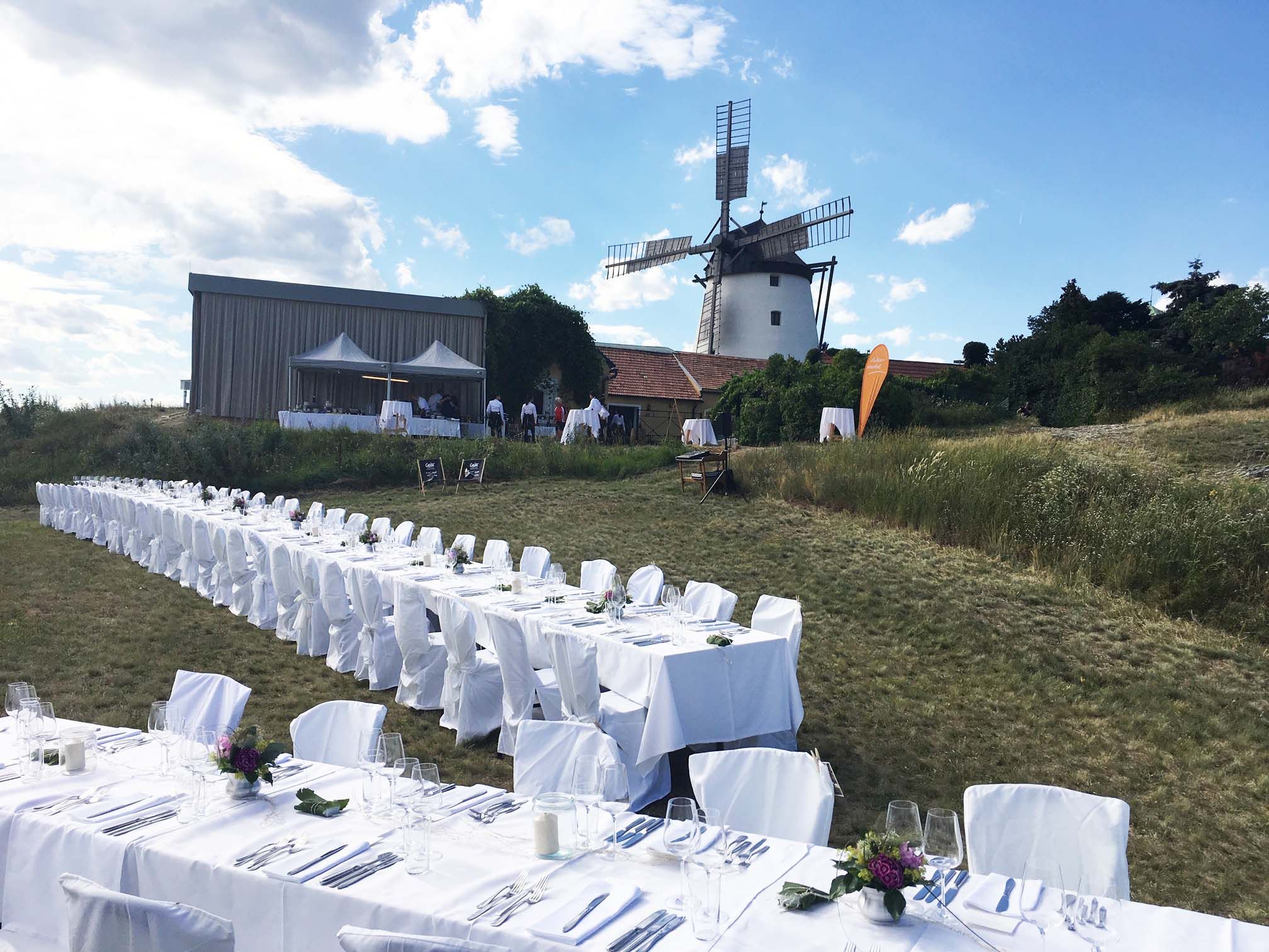 Lange Tafel im Freien mit Windmühle im Hintergrund.